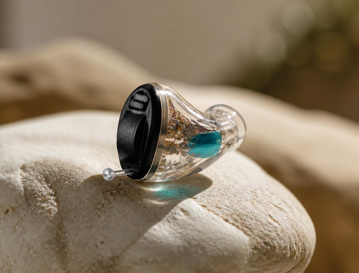 Close-up of a modern discreet receiver-in-canal hearing aid on a pale stone surface